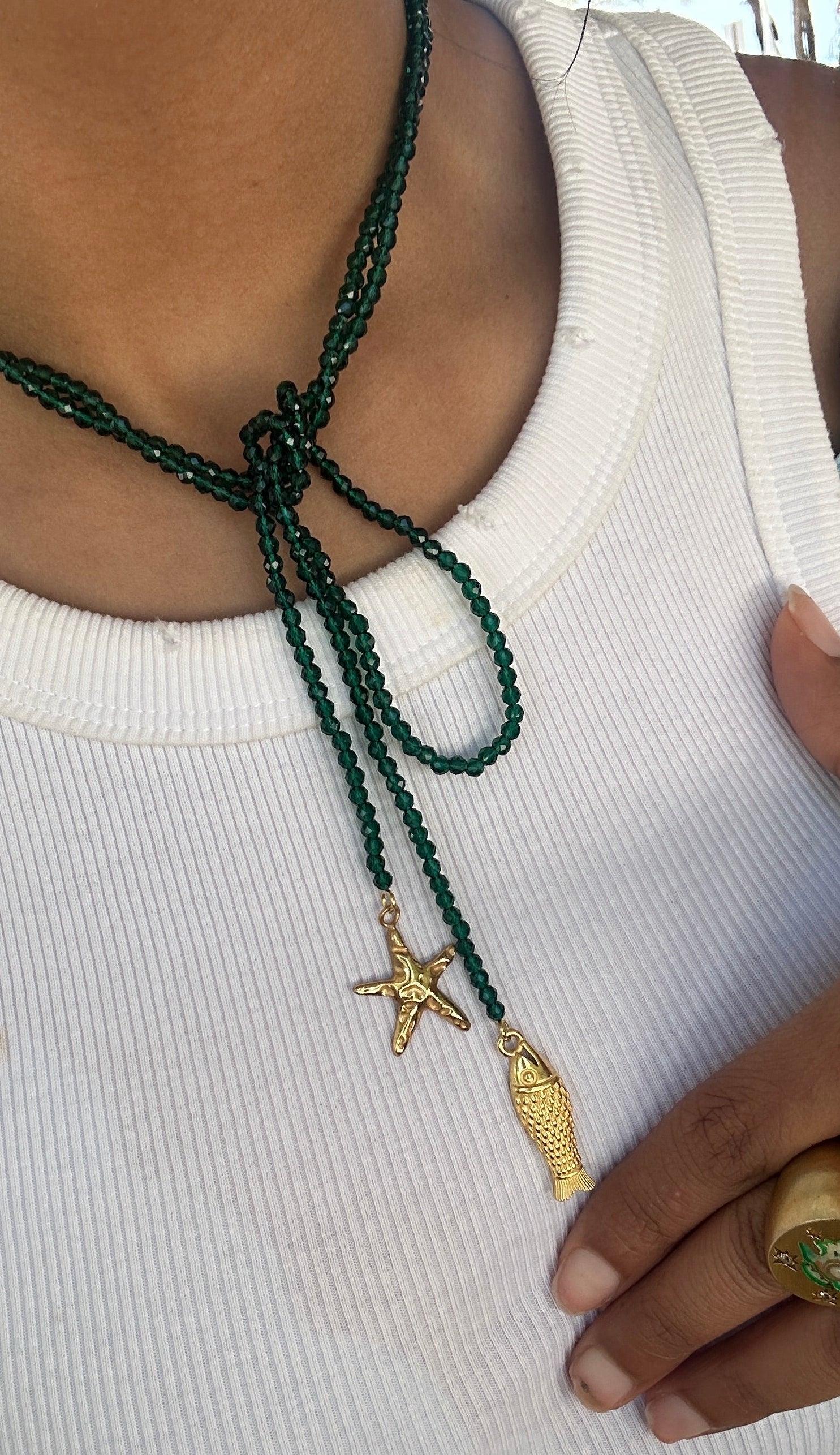 


Person wearing a green beaded necklace with starfish and leaf pendants on a white sleeve.
